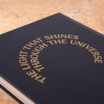 The back of the The Light That Shines... notebook. A black notebook featuring the statue's name in large concentric circles.