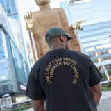 Man wearing The Light That Shines... Tee, facing the statue itself, so the title of the piece in gold across the back of the t-shirt is visible.