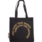 The Light That Shines... tote bag. A black tote featuring a screen print of the statue's name in large concentric circles. The bag also has a large branded woven tag with the High Line logo on it.