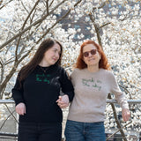 Mother and daughter stand amidst the serviceberry blooms on the High Line, holding hands. They're each wearing a Lingua Franca x High Line Sweater. The daughter is wearing the Maxine in Black and her mother is wearing the 100% Cashmere Sweater.