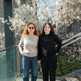 Mother and daughter standing at the 26th Street Overlook in front of the Serviceberry blossoms. Each wears a Lingua Franca x High Line Park in the Sky sweater. 