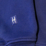 Closeup on the High Line icon, a railroad track inspired "H" on a small woven navy patch sewn onto the sleeve of the Park in the Sky Crewneck.