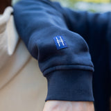 Closeup on High Line icon tag detail on the right sleeve of the Park in the Sky Crewneck Sweatshirt in navy.
