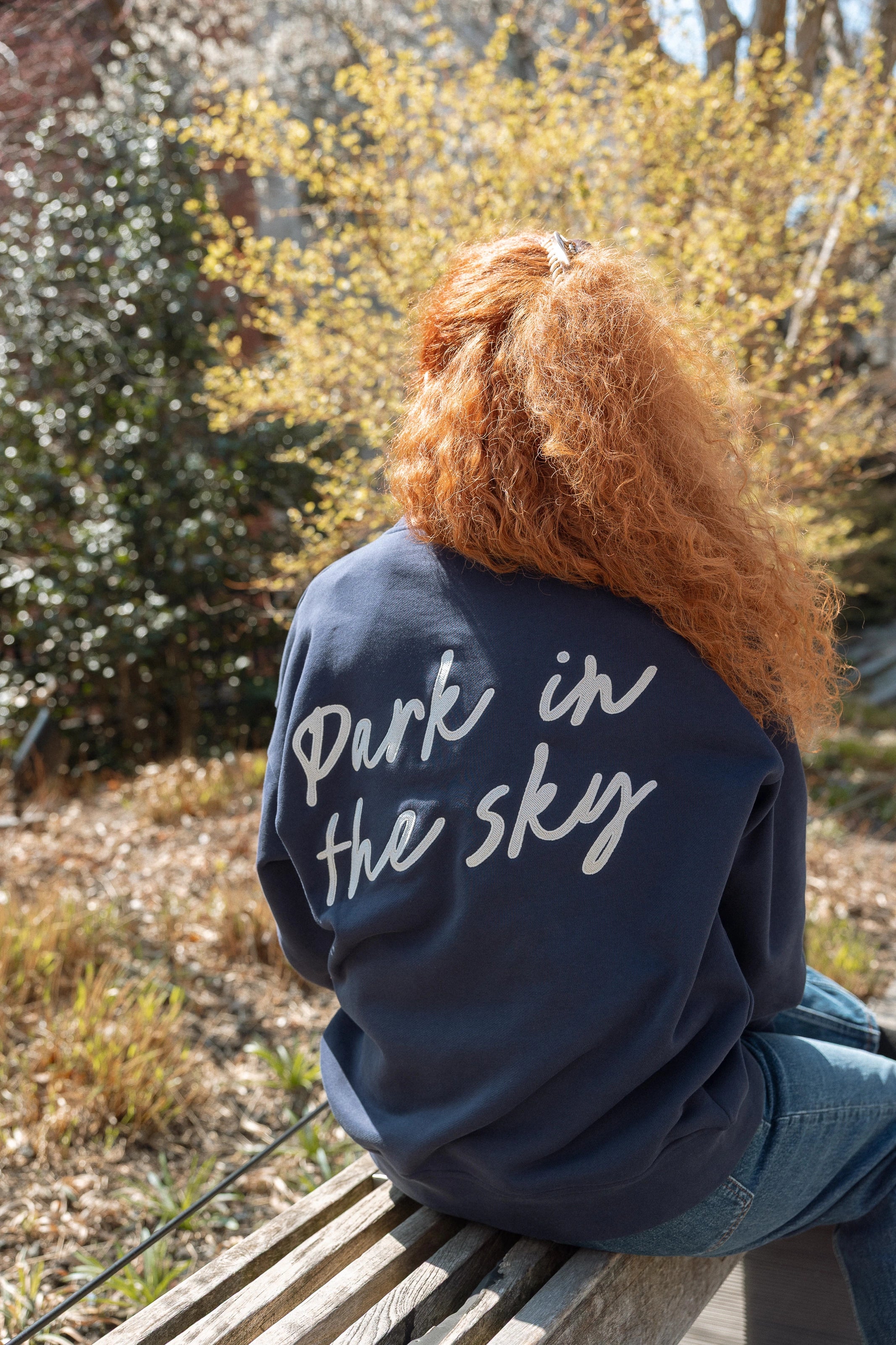 Woman wearing Park in the Sky Crewneck while sitting on the High Line.