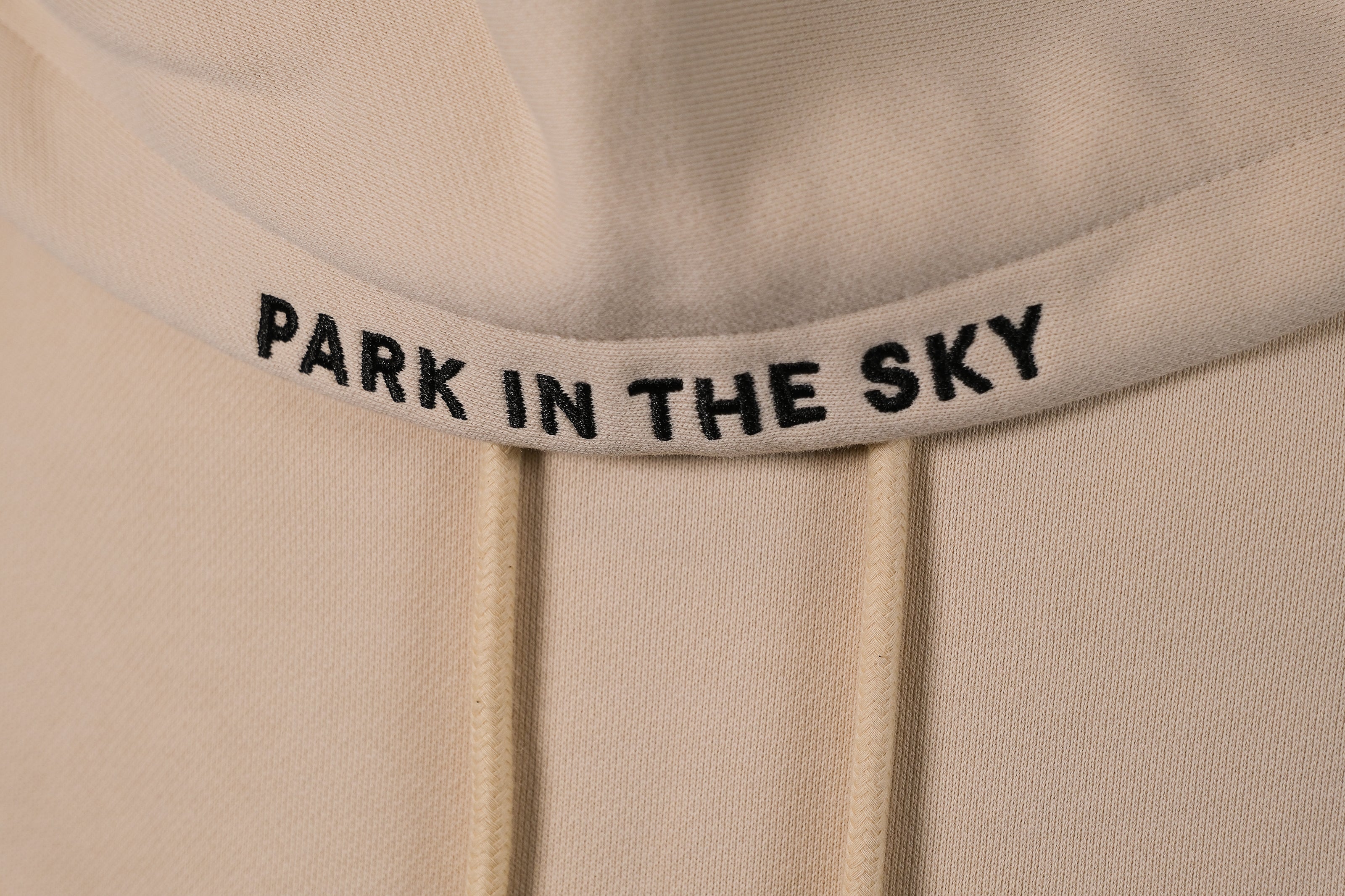 Park in the Sky embroidered hoodie in River Birch. Closeup of "PARK IN THE SKY" embroidered on the hood along the seam.