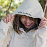 Woman wearing Park in the Sky hoodie, pulling the hood up so the "Park in the Sky" embroidery detail on the hood is visible.