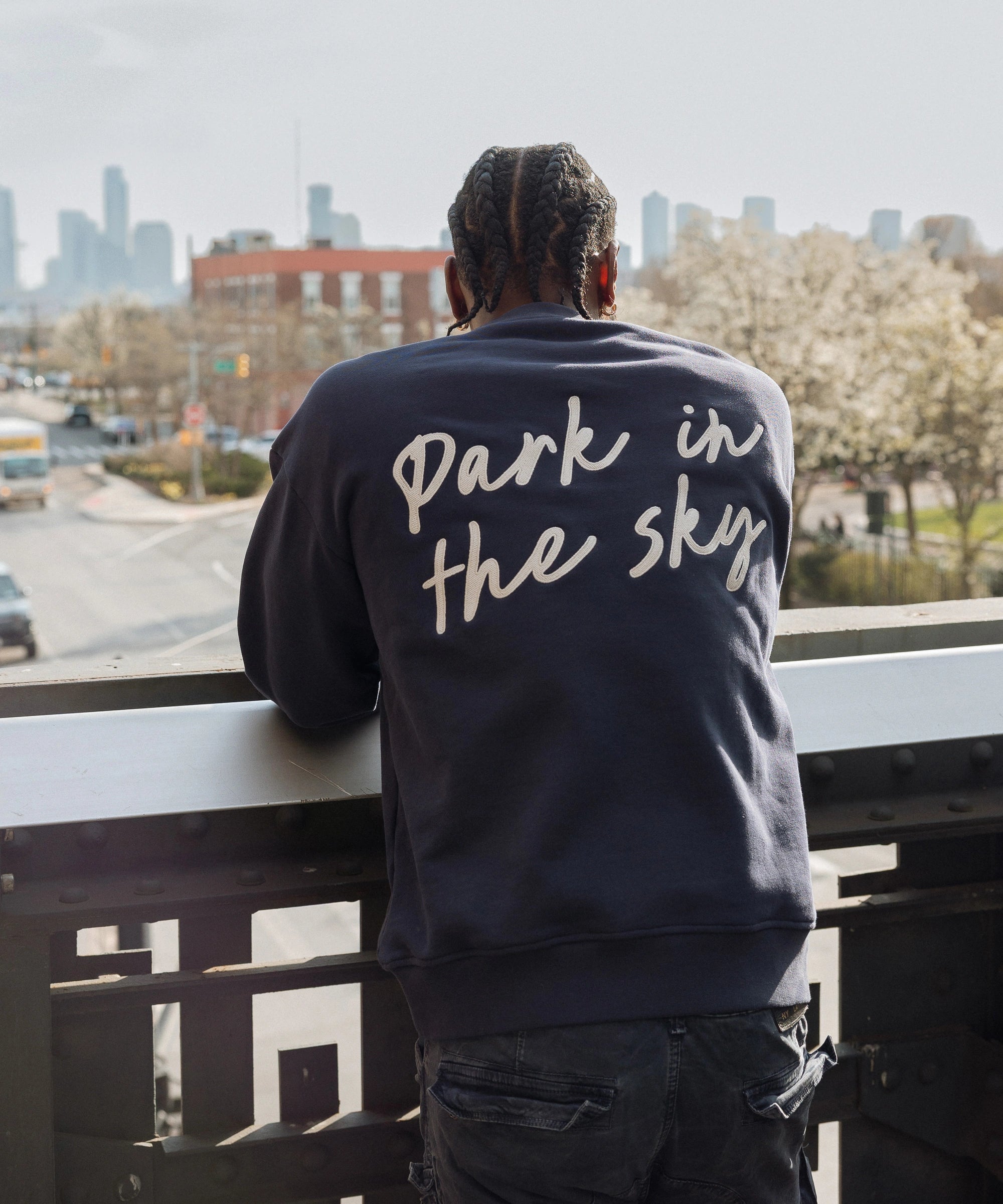 Man wearing Park in the Sky Crewneck in navy and looking out at the city from the High Line.