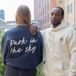 Woman wearing Park in the Sky crewneck and man in the Park in the Sky hoodie, with crewneck back details and front icon embroidery on the hoodie visible.