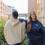 Woman wearing Park in the Sky crewneck and man in the Park in the Sky hoodie, with crewneck front and hood detail embroidery on the hoodie visible.