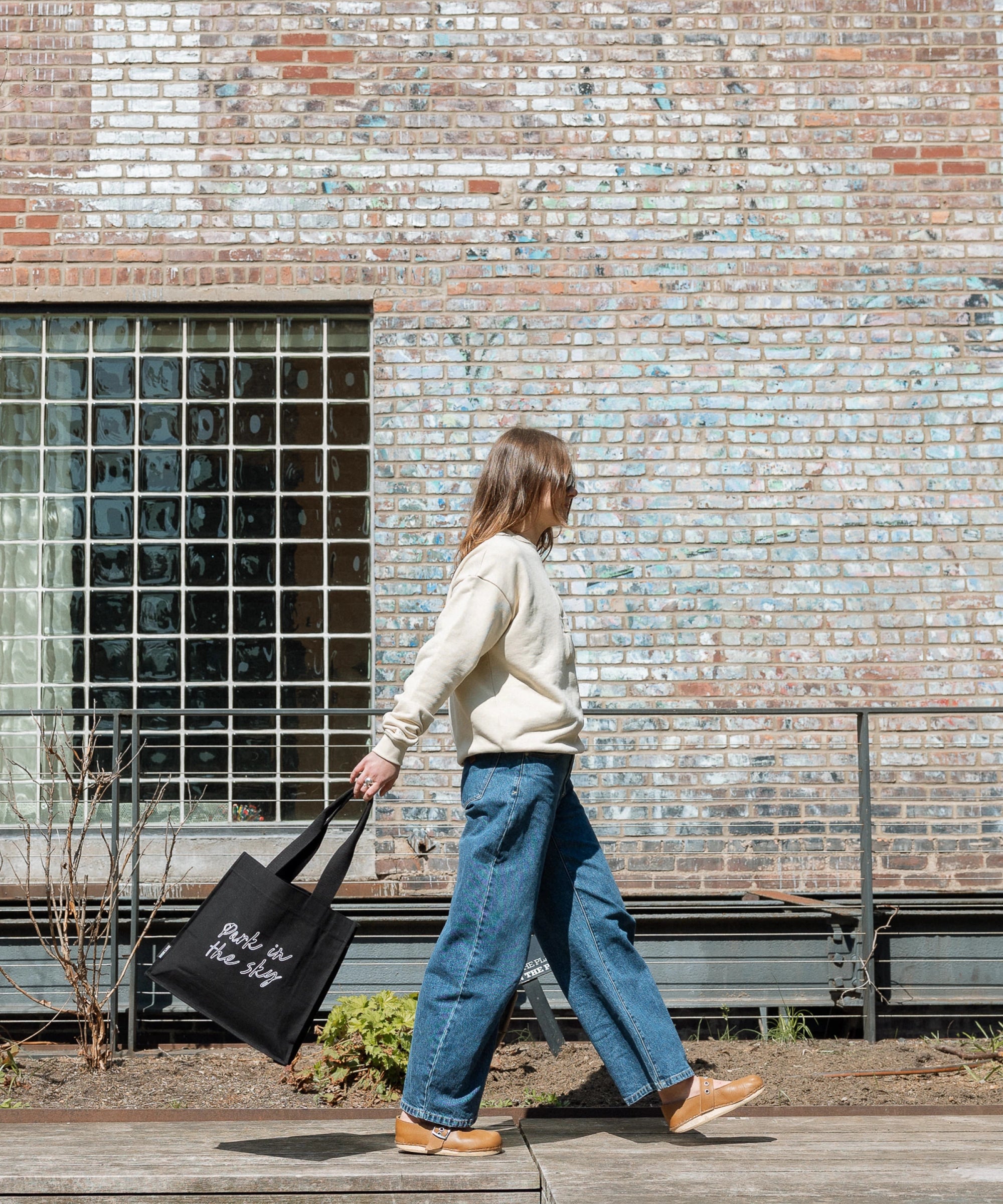 Woman walking along the High Line, swinging the Park in the Sky Tote.