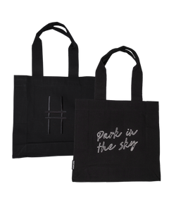Both sides of the Park in the Sky Tote in Black—one side features the tagline "park in the sky" embroidered in white and the other the railroad track "H" icon embroidered in black against black canvas with black straps.