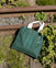 Park in the Sky Tote in Ivy with all the Community in the Sky collection pins on it, resting against the railroad tracks of the High Line.