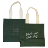Both sides of the Park in the Sky Tote in Ivy—one side features the tagline "park in the sky" embroidered in white and the other the railroad track "H" icon embroidered in dark green against the dark Ivy green canvas with natural straps.