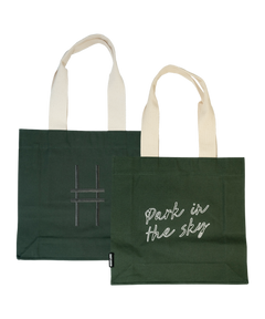 Both sides of the Park in the Sky Tote in Ivy—one side features the tagline "park in the sky" embroidered in white and the other the railroad track "H" icon embroidered in dark green against the dark Ivy green canvas with natural straps.