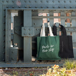 Park in the Sky Tote in Ivy and Park in the Sky Tote in Black hanging off of the railing of the High Line.