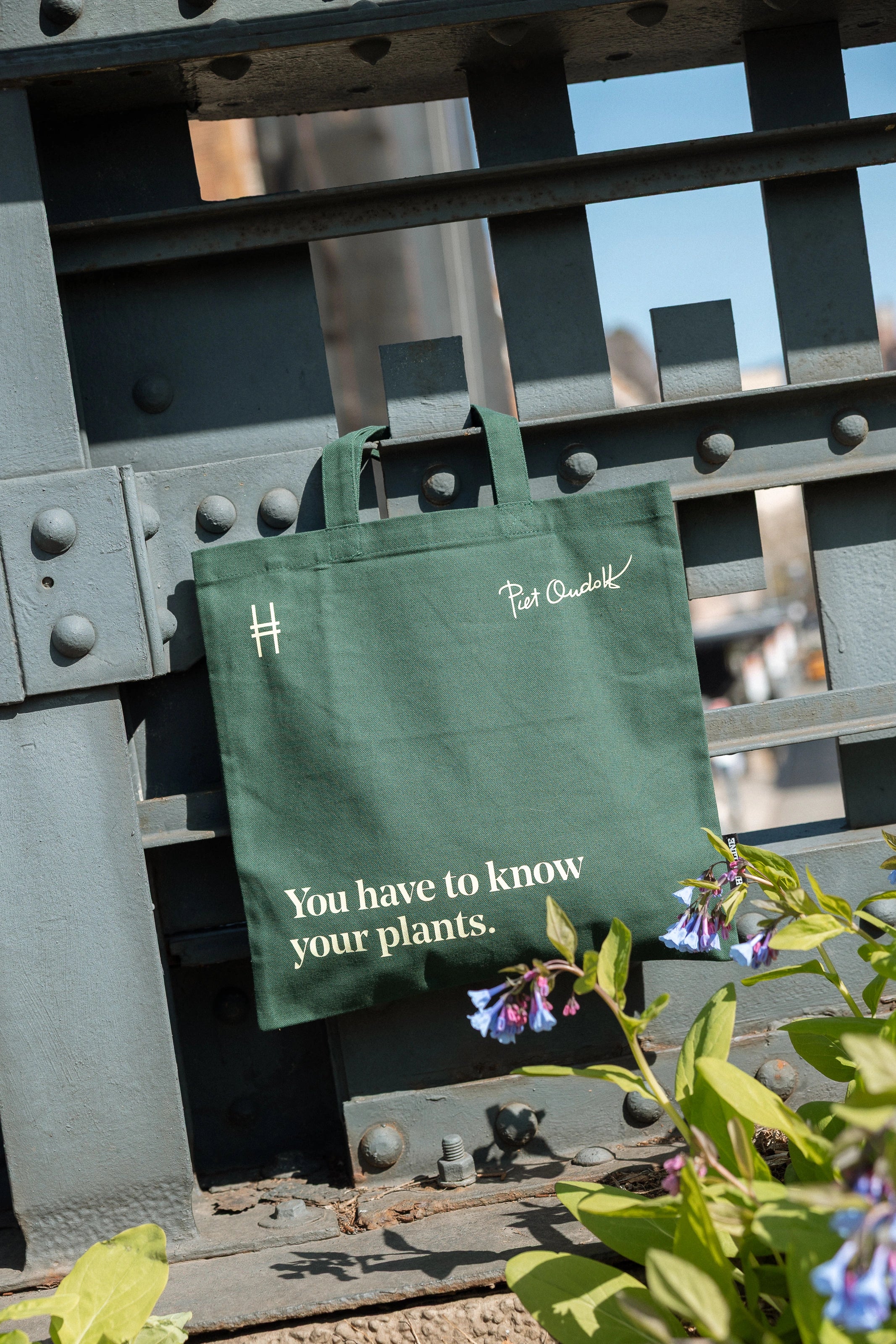 Piet Oudolf quote tote in Ivy, featuring the quote "You have to know your plants" hanging off of the rail of the High Line, flowers around it.