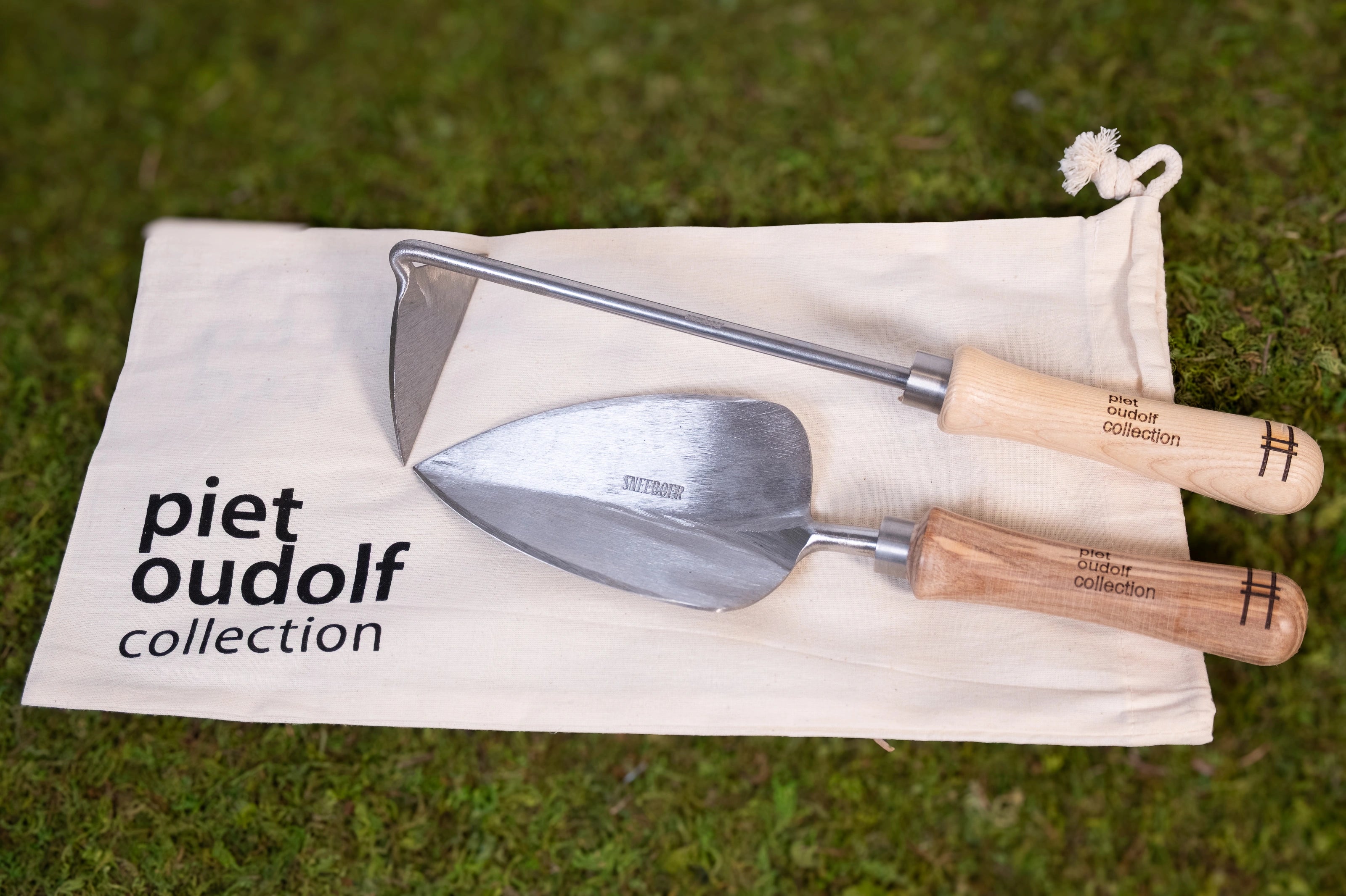 Sneeboer trowel and hand hoe with High Line icon and "Piet Oudolf collection" embossed on the wood handles shown on the carrying bag against moss.