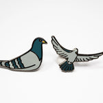The Pigeon Pins—two enamel pigeon pins, one sitting and one in flight—on a white background.