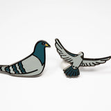 The Pigeon Pins—two enamel pigeon pins, one sitting and one in flight—on a white background.
