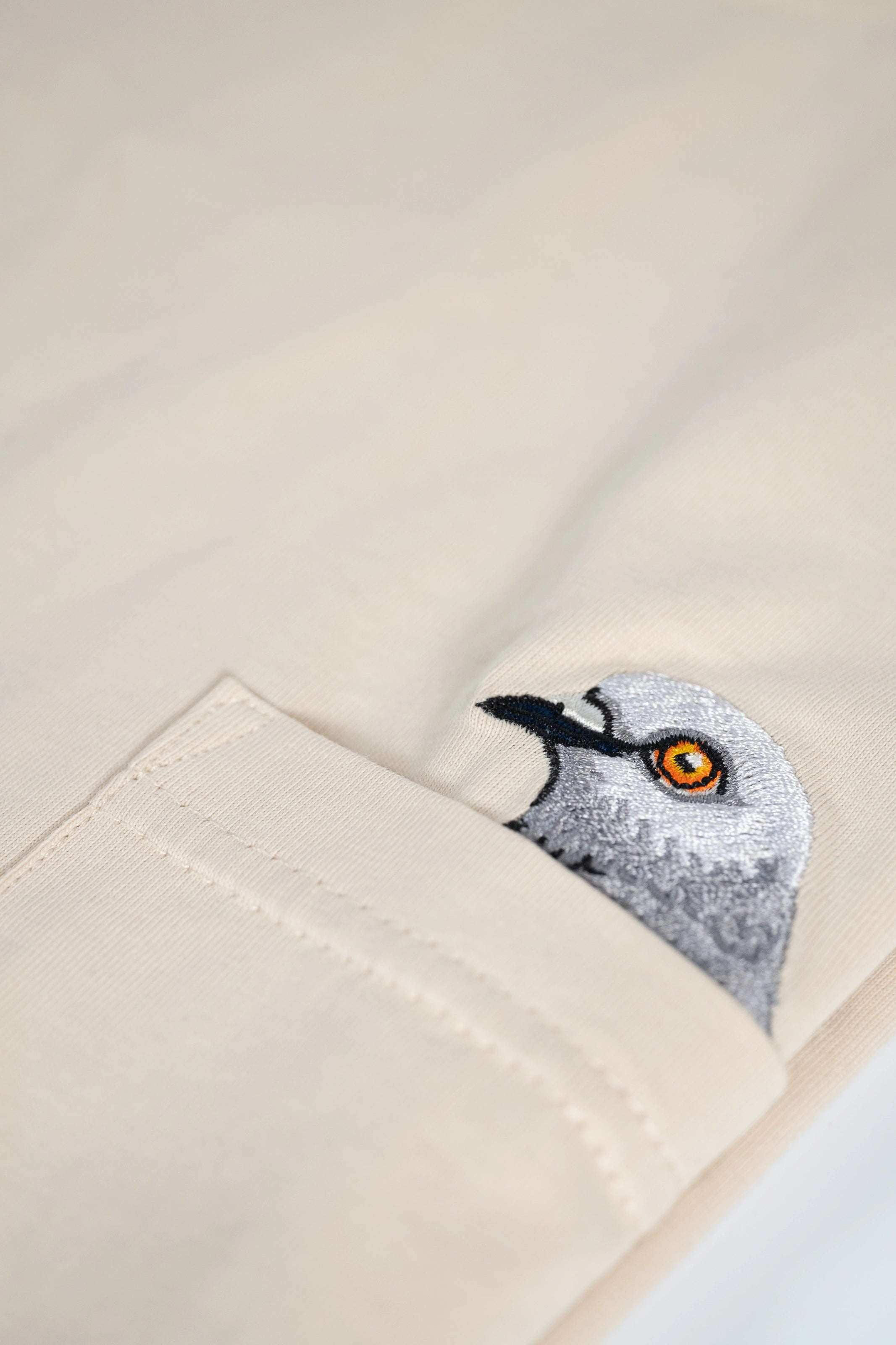 Pigeon Pocket tee—detailed shot of chest pocket featuring a small embroidered pigeon head poking out of it. 