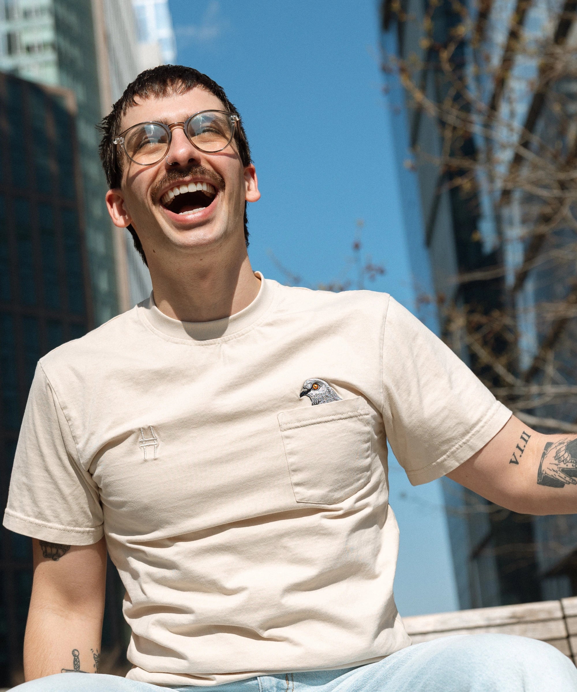 Person sitting on the High Line and laughing, wearing the Pigeon Pocket tee.