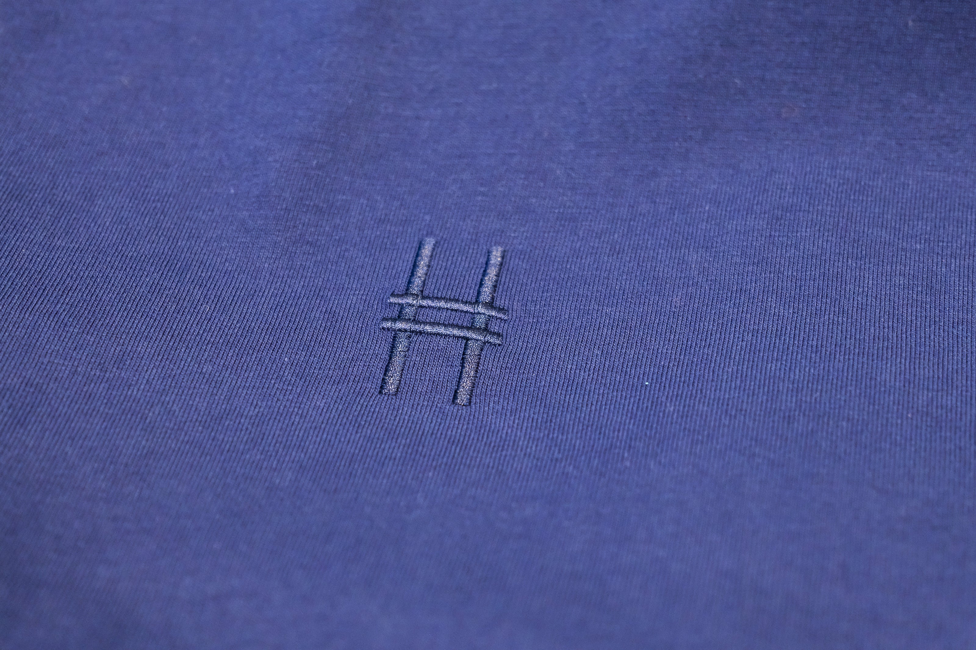 Closeup of the High Line icon, a railroad track inspired "H" embroidered on the Pigeon Pocket Longsleeve Tee in Navy.