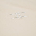 Closeup of the High Line icon, a railroad-track-inspired "H" which is embroidered in off-white thread to match the natural, 100% cotton fabric of the Pigeon Pocket long-sleeve tee in River Birch.