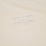 Closeup of the High Line icon, a railroad-track-inspired "H" which is embroidered in off-white thread to match the natural, 100% cotton fabric of the Pigeon Pocket long-sleeve tee in River Birch.