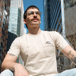 Person wearing the Pigeon Pocket tee—they sit at the Spur where the Dinosaur statue was, buildings and trees behind them.