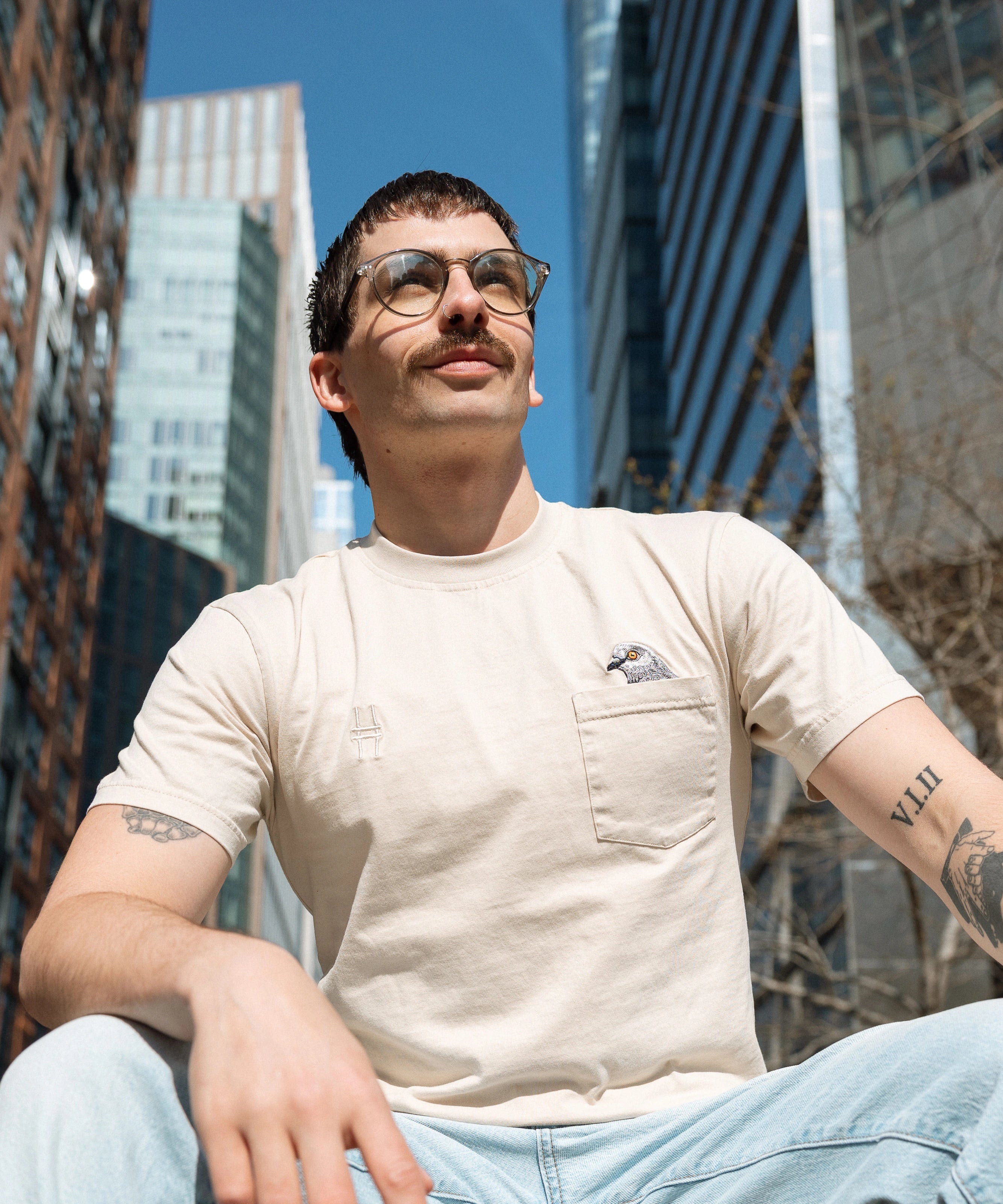 Person wearing the Pigeon Pocket tee—they sit at the Spur where the Dinosaur statue was, buildings and trees behind them.