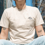 Person wearing the Pigeon Pocket tee, their legs and face cropped out so we focus on their torso and the embroidery details.