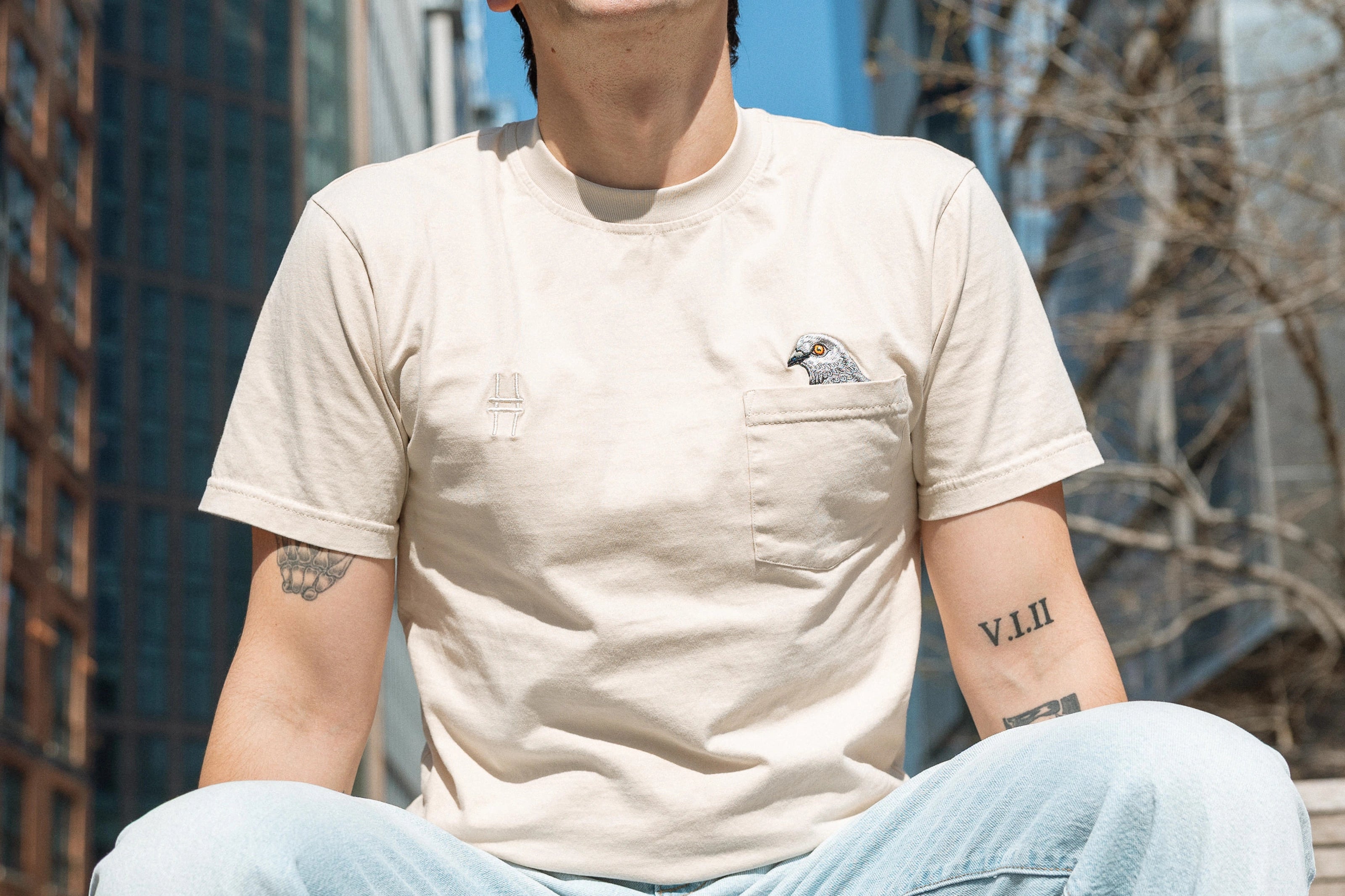 Person wearing the Pigeon Pocket tee, their legs and face cropped out so we focus on their torso and the embroidery details.