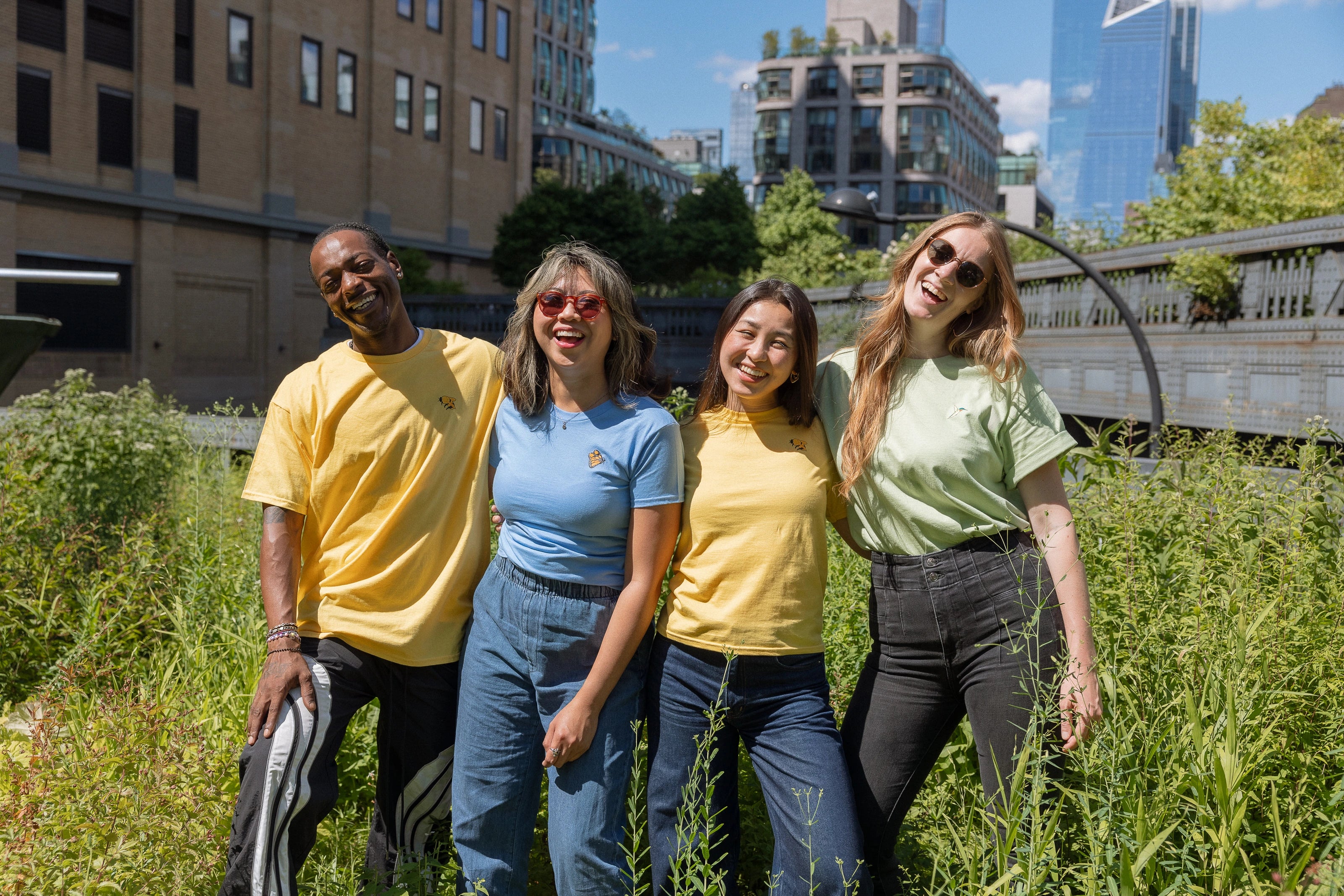 Four people in Protect Pollinators Tees standing amongst the foliage on the High Line, smiling and laughing.