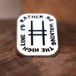 Enamel pin with text 'I'd Rather Be Walking The High Line' resting on wood.