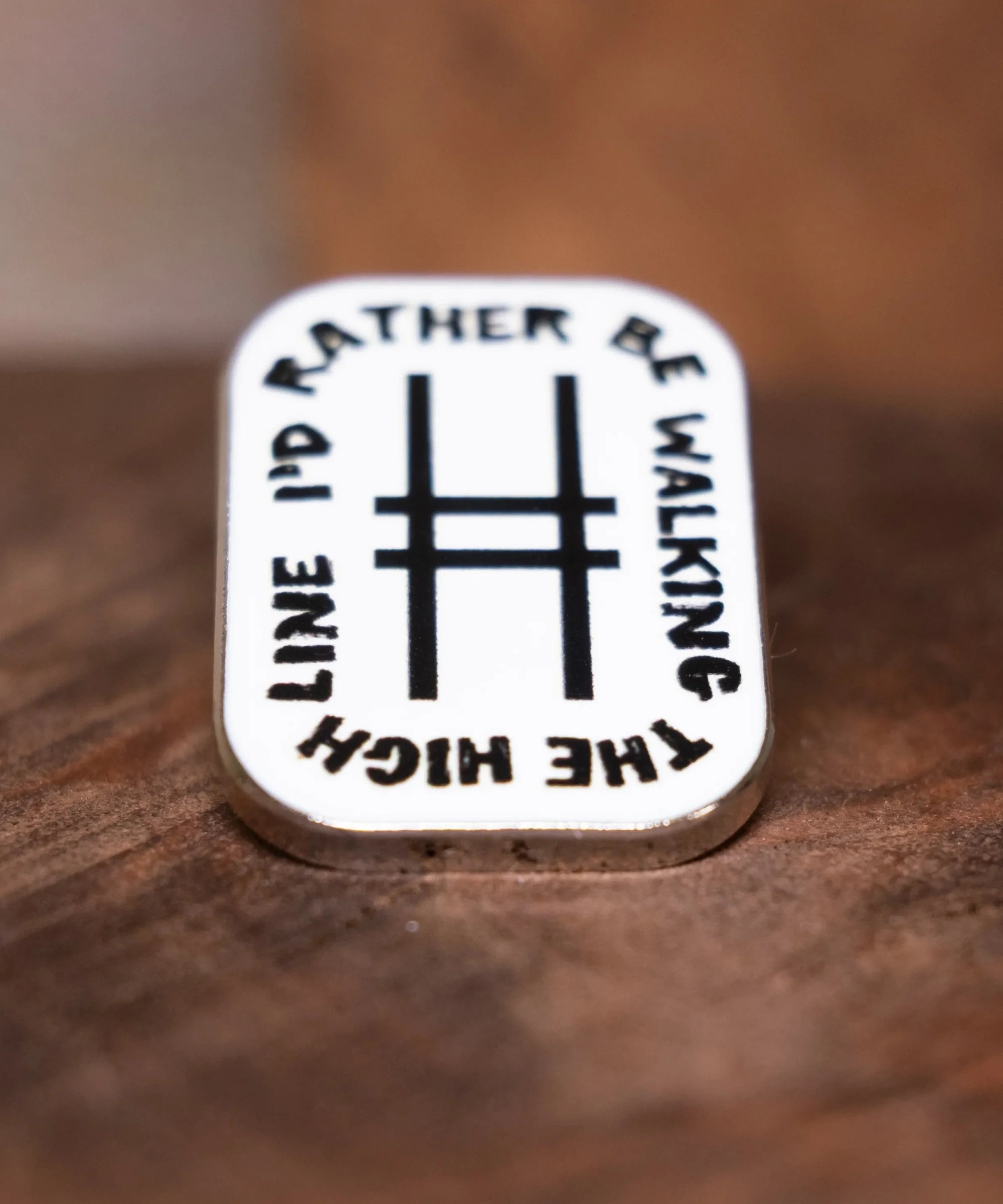 Enamel pin with text 'I'd Rather Be Walking The High Line' resting on wood.
