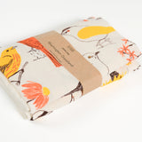 Claudia Pearson x High Line Washington Grassland tea towel, folded and wrapped in a kraft paper band. The flour sack cotton tea towel is covered in illustrations of birds and plants that populate the High Line in browns, yellows and oranges.