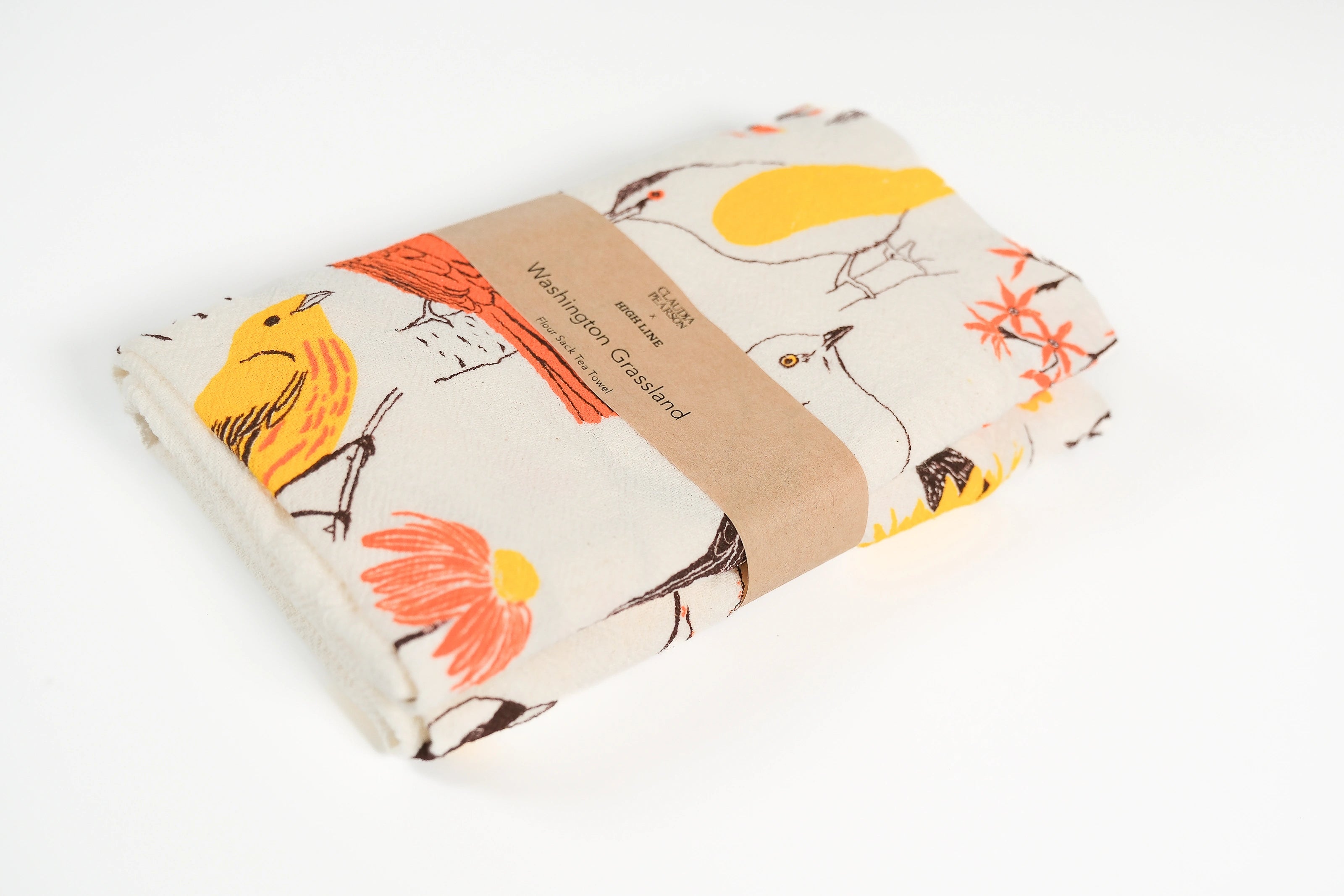 Claudia Pearson x High Line Washington Grassland tea towel, folded and wrapped in a kraft paper band. The flour sack cotton tea towel is covered in illustrations of birds and plants that populate the High Line in browns, yellows and oranges.