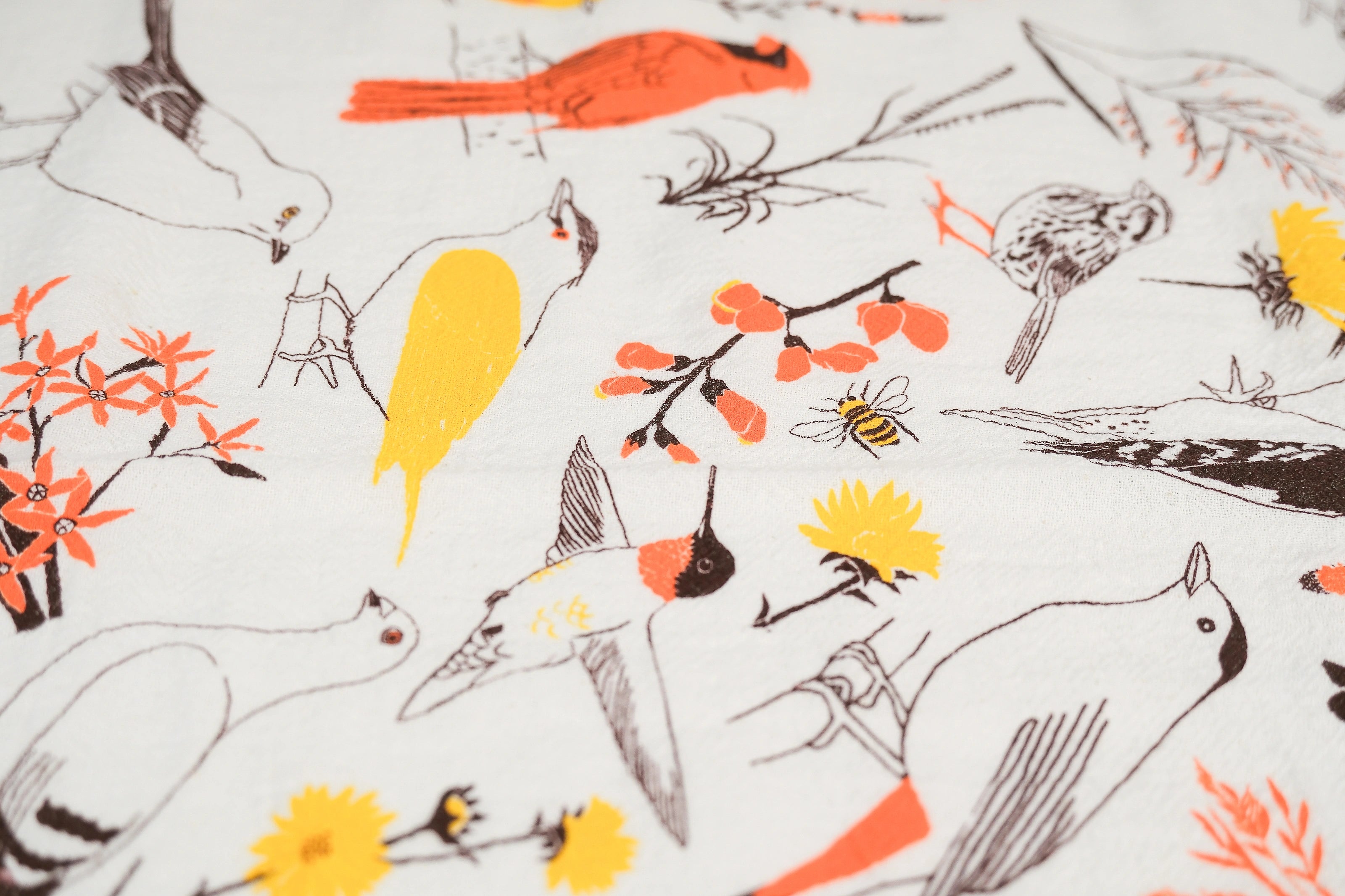 Closeup of the Claudia Pearson x High Line Washington Grassland tea towel. The flour sack cotton tea towel is covered in illustrations of birds and plants that populate the High Line in browns, yellows and oranges.