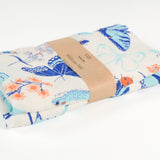 Claudia Pearson x High Line Wildflower Field tea towel, folded and wrapped in a kraft paper band. The flour sack cotton tea towel is covered in illustrations of butterflies, ladybugs, moths, other insects and wildflowers in blues and oranges.