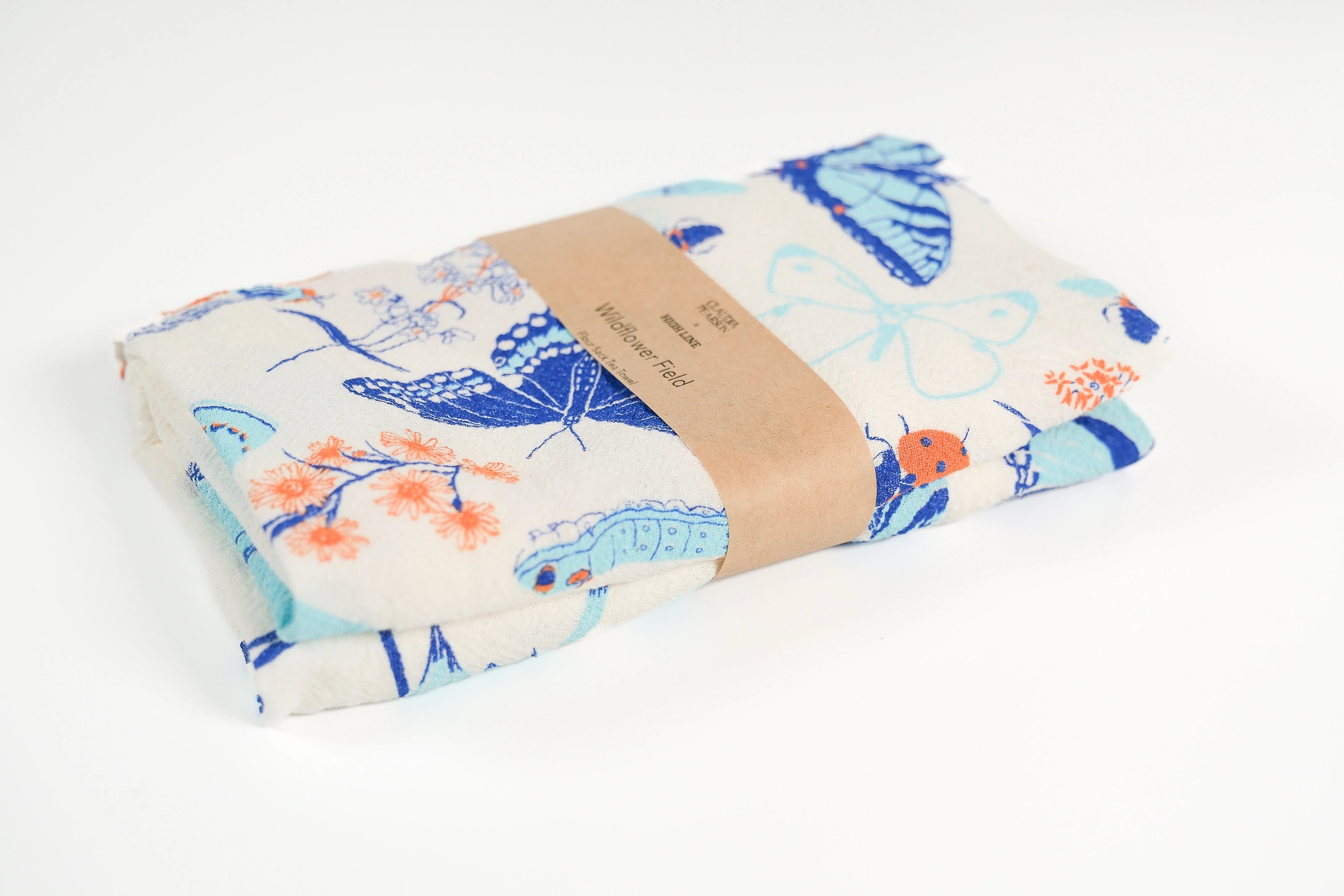 Claudia Pearson x High Line Wildflower Field tea towel, folded and wrapped in a kraft paper band. The flour sack cotton tea towel is covered in illustrations of butterflies, ladybugs, moths, other insects and wildflowers in blues and oranges.