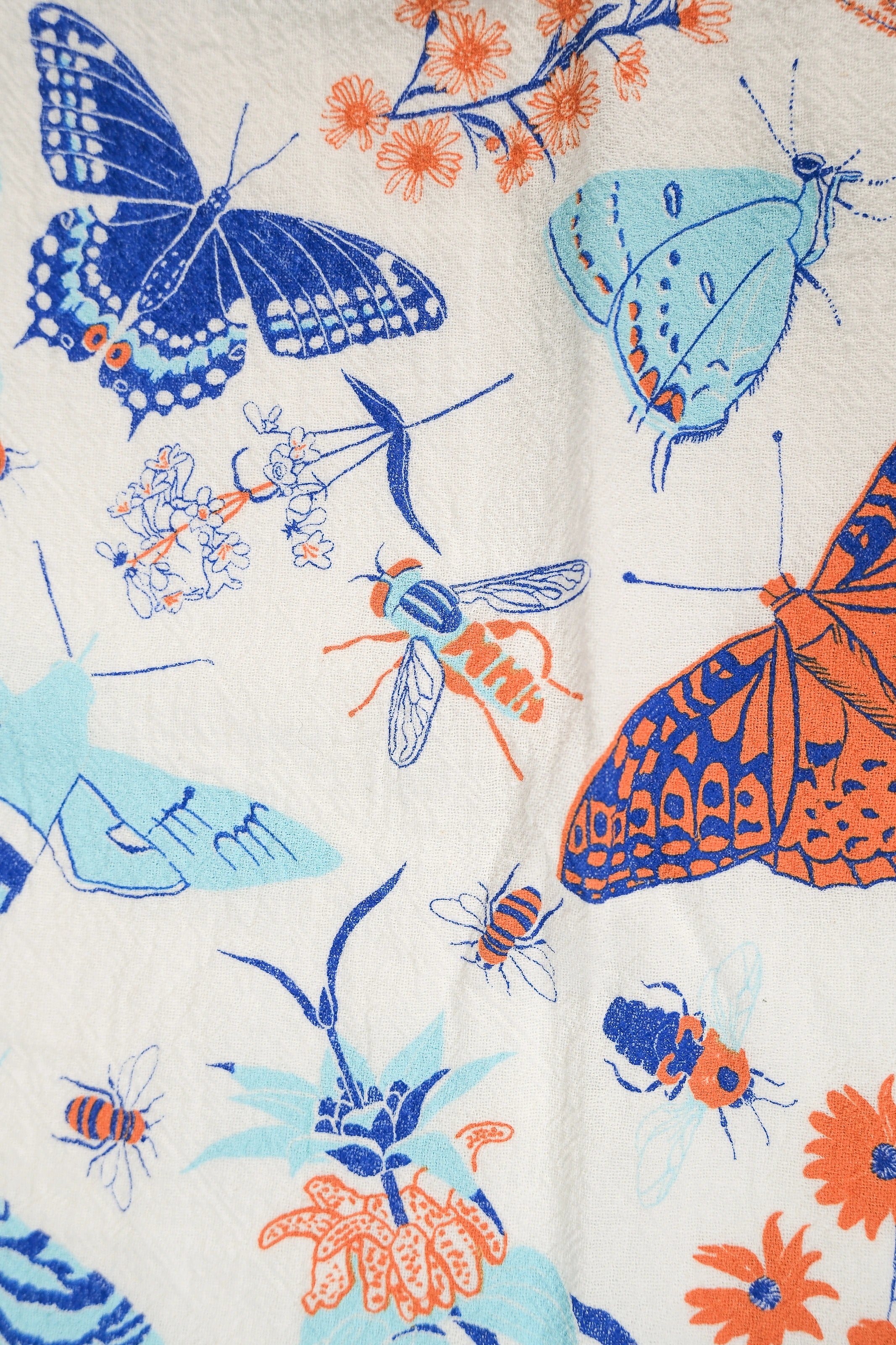Claudia Pearson x High Line Wildflower Field tea towel, shown in detail. The flour sack cotton tea towel is covered in illustrations of butterflies, ladybugs, moths, other insects and wildflowers in blues and oranges.